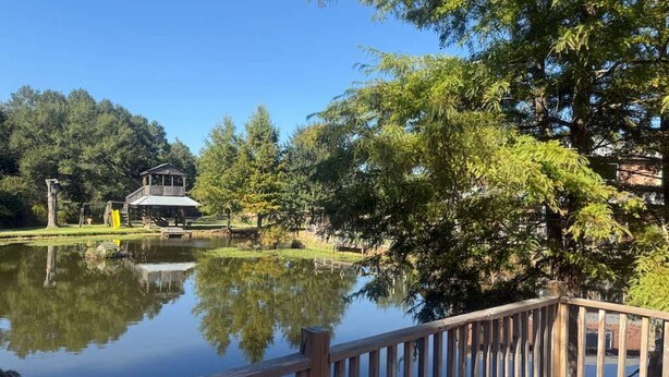 Une terrasse en bois surplombant un lac paisible, avec un belvédère et des arbres en arrière-plan.