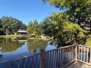 A wooden deck overlooking a calm lake with a gazebo and trees in the background. - Cozy Retreat Home - Oak (Tomball)