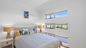 Un dormitorio con cama, dos mesitas de noche, dos lámparas, un cuadro en la pared y una ventana con vistas a zonas verdes.