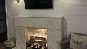 Ein Wohnzimmer mit weißer Holzvertäfelung, einem flachbildfernseher über einem Kamin und zwei Wandlampen.