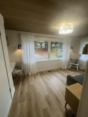 Una habitación con un ventanal grande, una silla, una mesita y una lámpara.