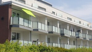 A multi-story residential building with balconies, a brick facade, and a green umbrella.