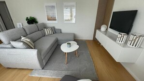 A modern living room with a grey sectional sofa, a small round table, and a flat-screen TV mounted on the wall.