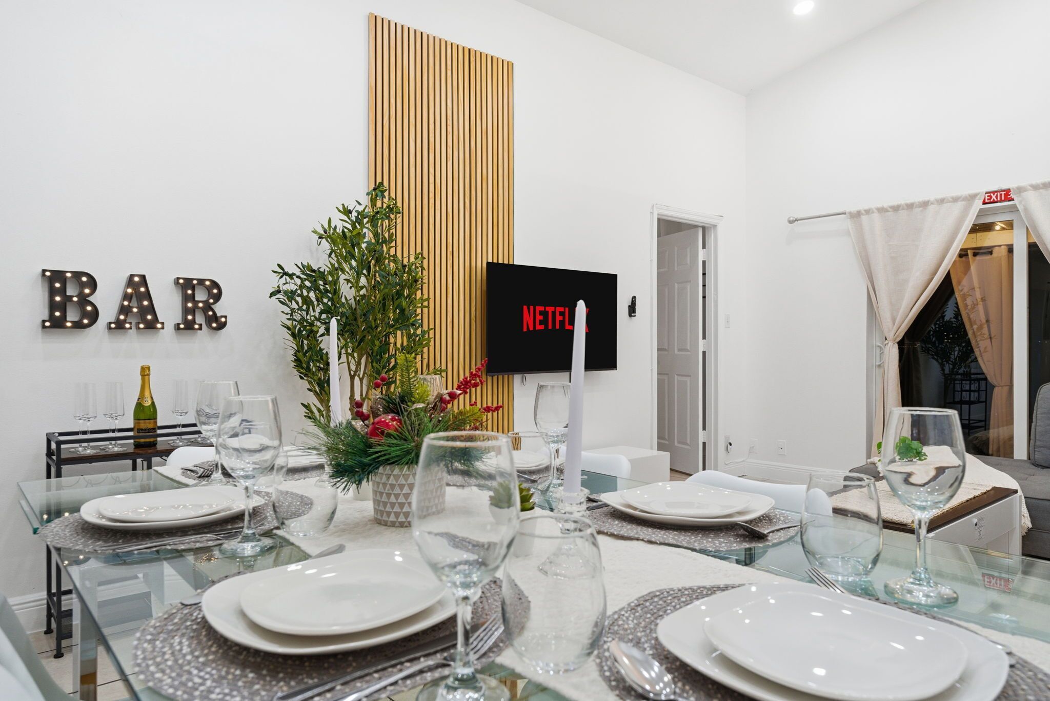 Ein Essbereich mit einem Glastisch, gedeckt für sechs Personen, einem 'BAR'-Schild, einem Netflix-Schild und einer Wandpaneelaus Holz.