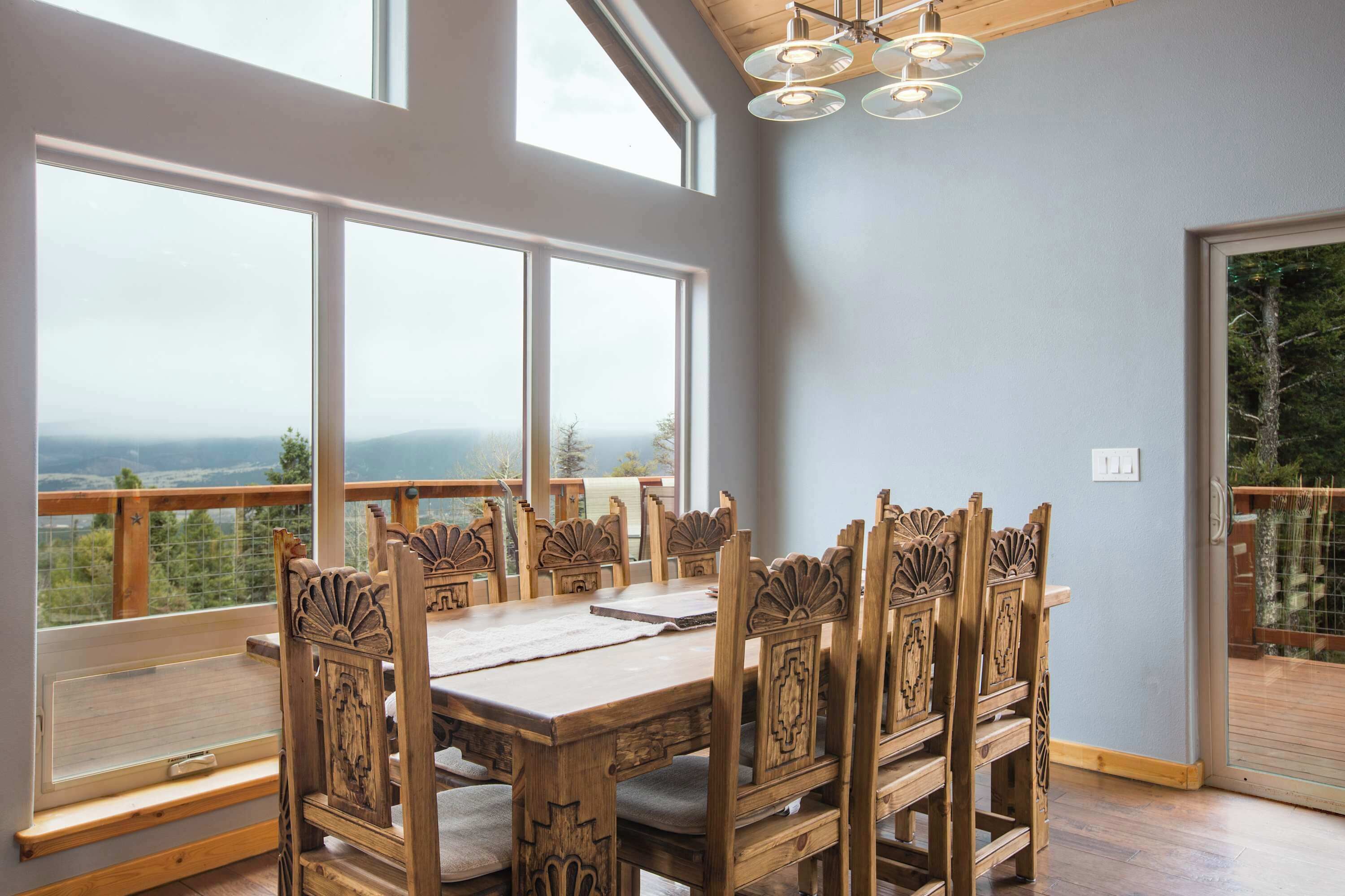 A dining area with a wooden table and chairs, large windows, and a view of the outdoors.