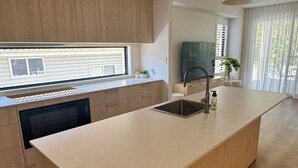 Een moderne keuken met houten kastjes, een centraal eiland met een spoelbak, hangende verlichting en uitzicht op de omgeving.