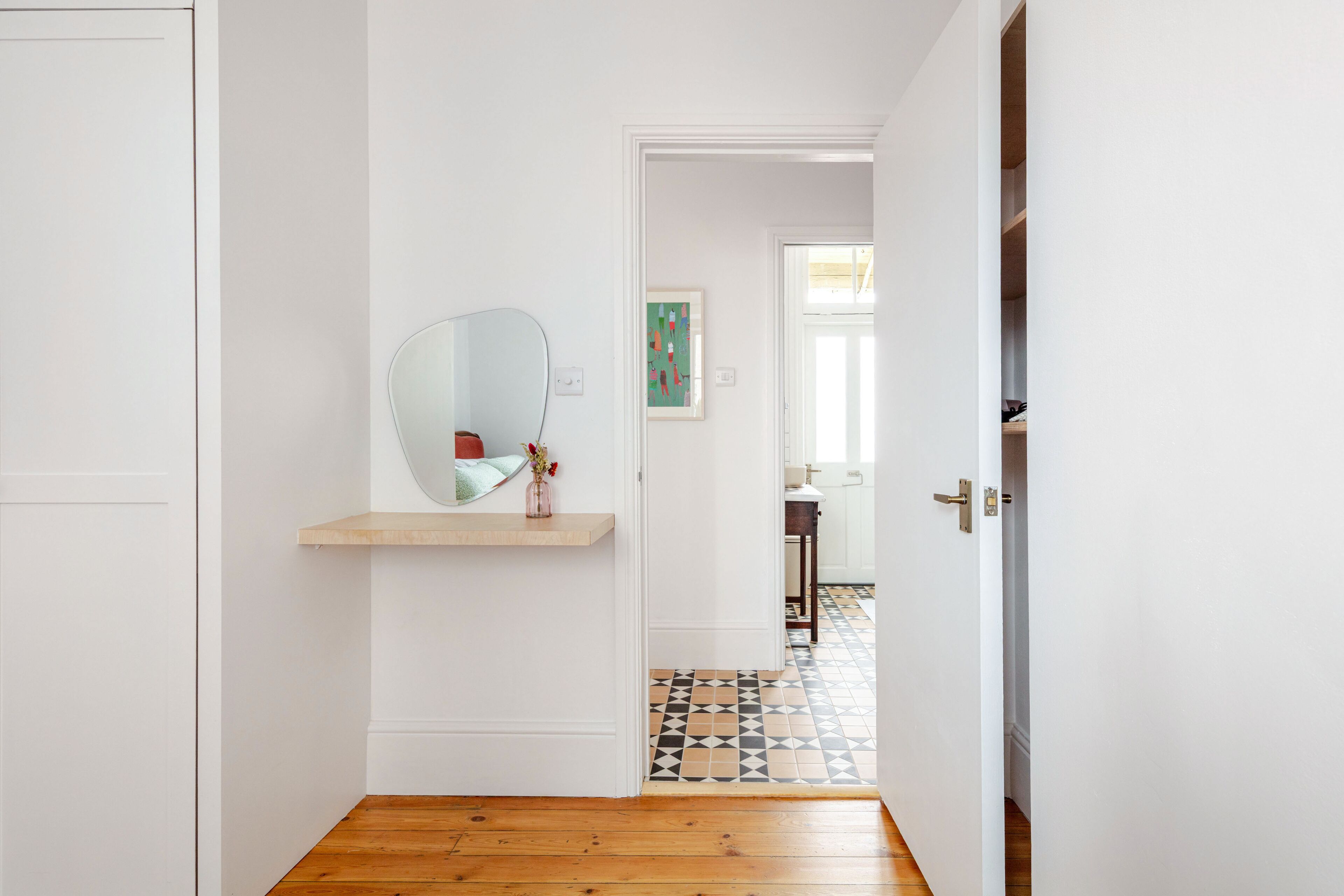 A hallway with a wooden floor, a white door, and a mirror on a wall.