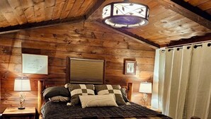 A cozy wooden bedroom with a bed, two bedside tables, a hanging light fixture, and a window with curtains. - 130 Feet of Lakefront with Unforgettable Views and Access (Plattsburgh)