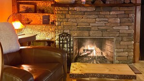 A cozy living room with a stone fireplace, a leather sofa, a wooden coffee table, and a wall-mounted shelf with decorative items. - 130 Feet of Lakefront with Unforgettable Views and Access (Plattsburgh)