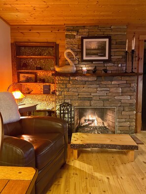 A cozy living room with a stone fireplace, a leather sofa, a wooden coffee table, and a wall-mounted shelf with decorative items.