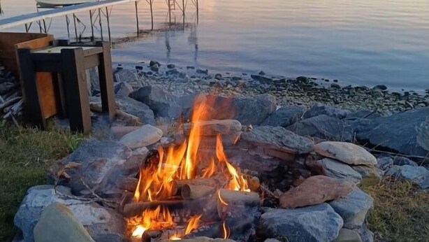 A campfire surrounded by rocks, a dock with chairs, and a calm lake with mountains in the distance. - 130 Feet of Lakefront with Unforgettable Views and Access (Plattsburgh)