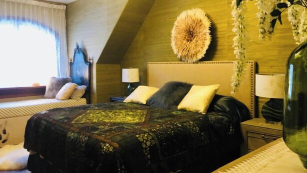 A bedroom with a sloped ceiling, a bed with a patterned bedspread, two bedside lamps, and a large decorative wall piece. - Cozy Nature-Inspired Feather Room With King Bed, Alcove Nook (Bigfork)