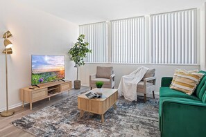 Un salon moderne avec un téléviseur à écran plat, un canapé vert, une table basse en bois et un lampadaire.