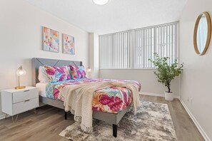 A bedroom with a bed, bedside table, lamp, wall art, window blinds, and a potted plant. - Luxurious & Spacious 1Bed 1Bath Apt In Santa Monica (Santa Monica)