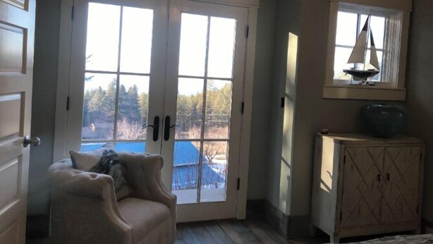 Una habitación con un amplio ventanal corredero que da a un paisaje nevado, un mueble bajo con un adorno de velero y un sillón con cojín.