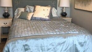 Una cama bien hecha con cubrecama acolchado, dos mesitas de noche con lámparas y una pared con un cuadro.