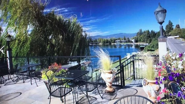 Un patio al aire libre con mesas y sillas, con vista a un lago y montañas.