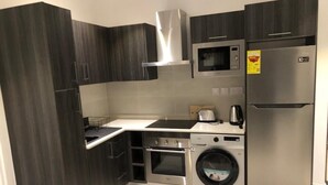 Eine kompakte Küche mit dunklen Holzschränken, einem Edelstahlkühlschrank, einer Mikrowelle, einem Backofen und einer integrierten Waschmaschine.