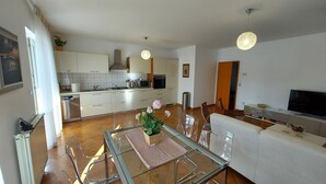 A modern kitchen with white cabinets, a dining area with a glass table, and a living room with a sofa and TV. - Marvelous 5-bedroom house with great terrace in Pješčana Uvala (Pješčana Uvala)