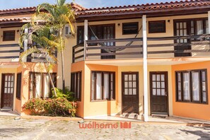 A two-story building with a balcony, a palm tree, and a flower bed. - Duplex em Porto Seguro com Acesso a Praia Axe Moi (Porto Seguro)