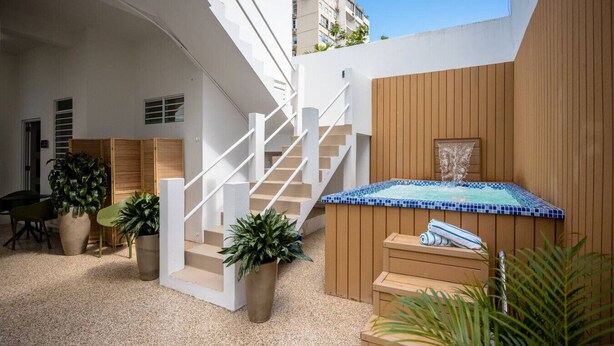 A modern outdoor area with a wooden staircase, a hot tub, and potted plants. - Urban Beach House「UNIT #202「Palma」 (San Juan)