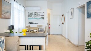 Ein modernes Wohnzimmer mit einer Couch, einem Esstisch mit Stühlen und einer Küchenzeile mit Arbeitsplatte sowie einem gelben Dekoelement.