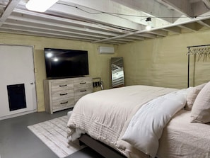 Une chambre à coucher avec un lit, une commode, un téléviseur, un miroir et une armoire.