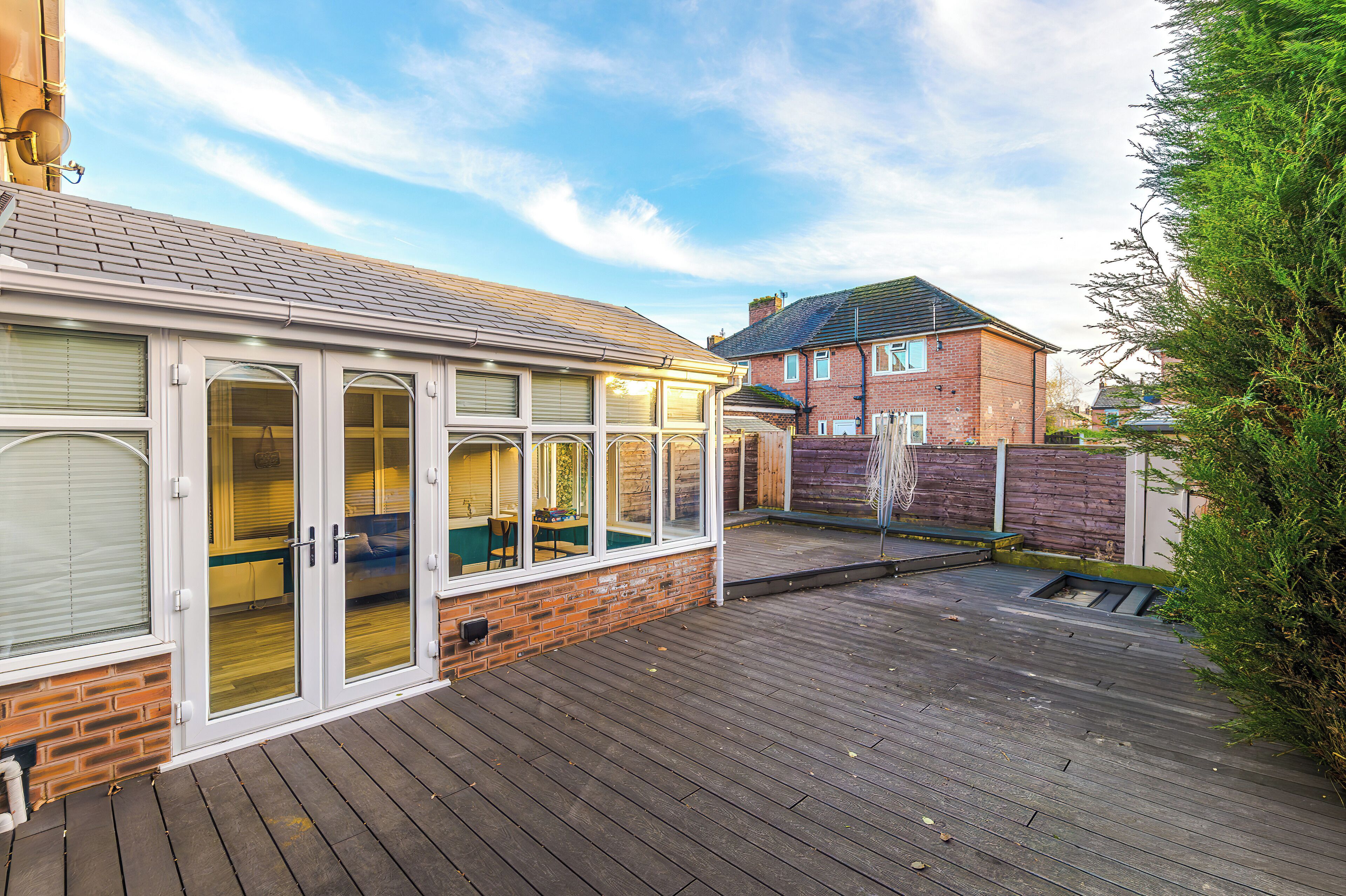 A wooden deck with a glass enclosure, a brick wall, and a brick house in the background.