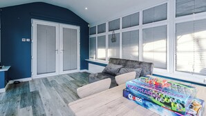 A room with a blue wall, a grey sofa, a wooden table, and a window with blinds. - Modern 3-Bed - Near Etihad & City Centre (Manchester)