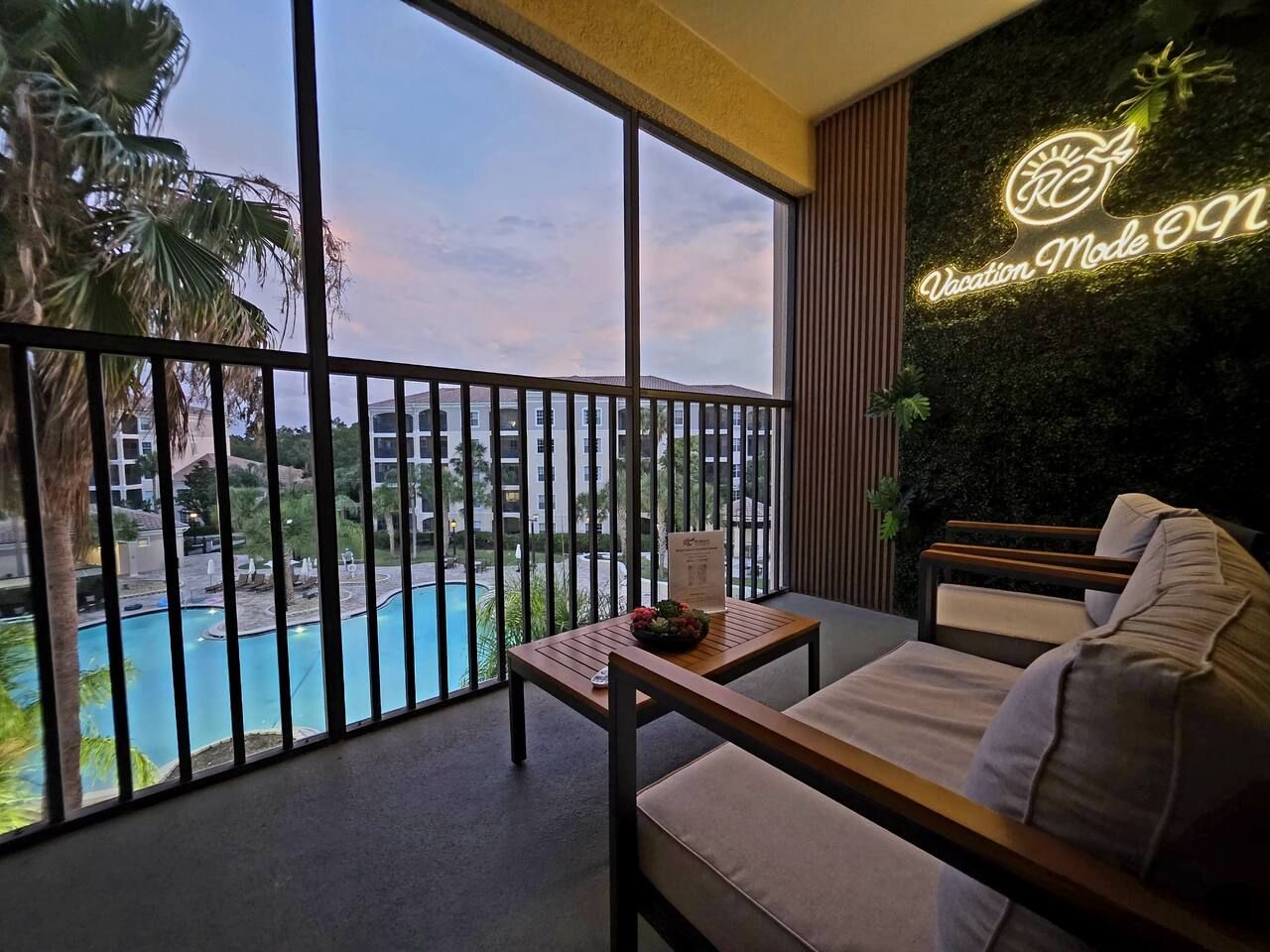 Een balkon met uitzicht op een zwembad en een neonbord waarop staat 'Vakantie modus AAN'.