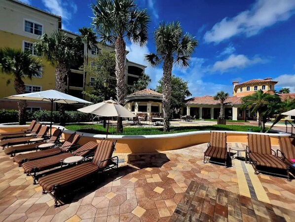 Ein Poolbereich eines Resorts mit Liegestühlen und Sonnenschirmen, umgeben von Palmen und Gebäuden.