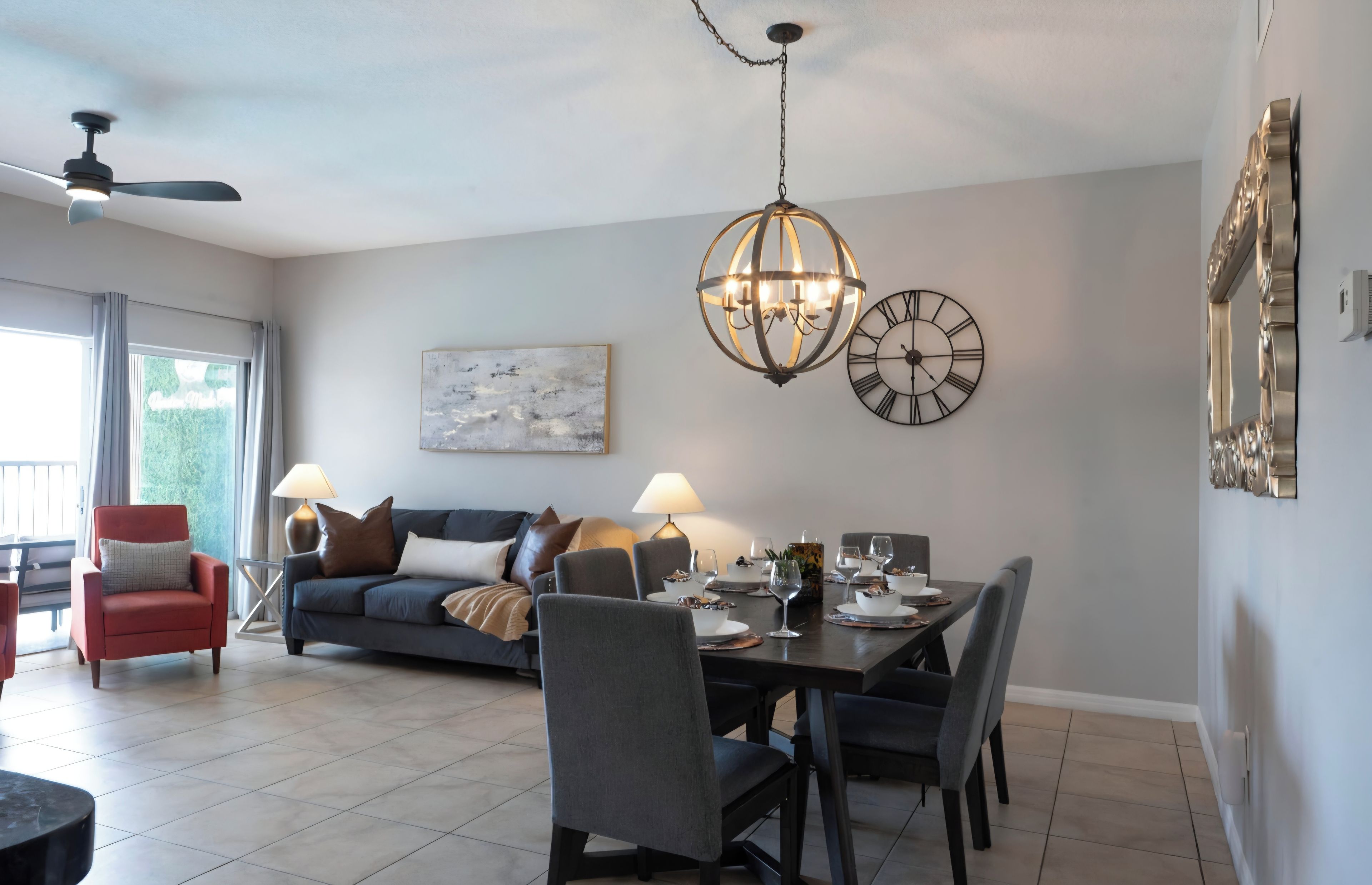 Un salon moderne avec un coin repas, agrémenté d’un ventilateur de plafond, d’un lustre et d’une horloge murale.