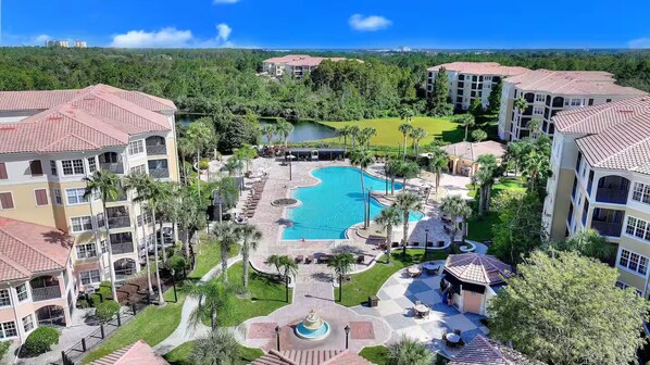 A resort with a central swimming pool, multiple buildings, and lush greenery. - Luxury Disney Escape • Private Balcony • Lake & Pool Views (Orlando)