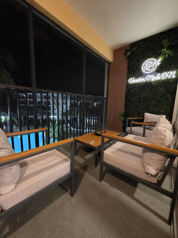 A balcony with two cushioned chairs and a small table, a neon sign reading 'Vacation Mode ON', and a view of a building at night. - Luxury Disney Escape • Private Balcony • Lake & Pool Views (Orlando)