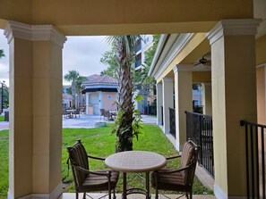 A covered patio with two chairs and a table, overlooking a courtyard with a building in the background.