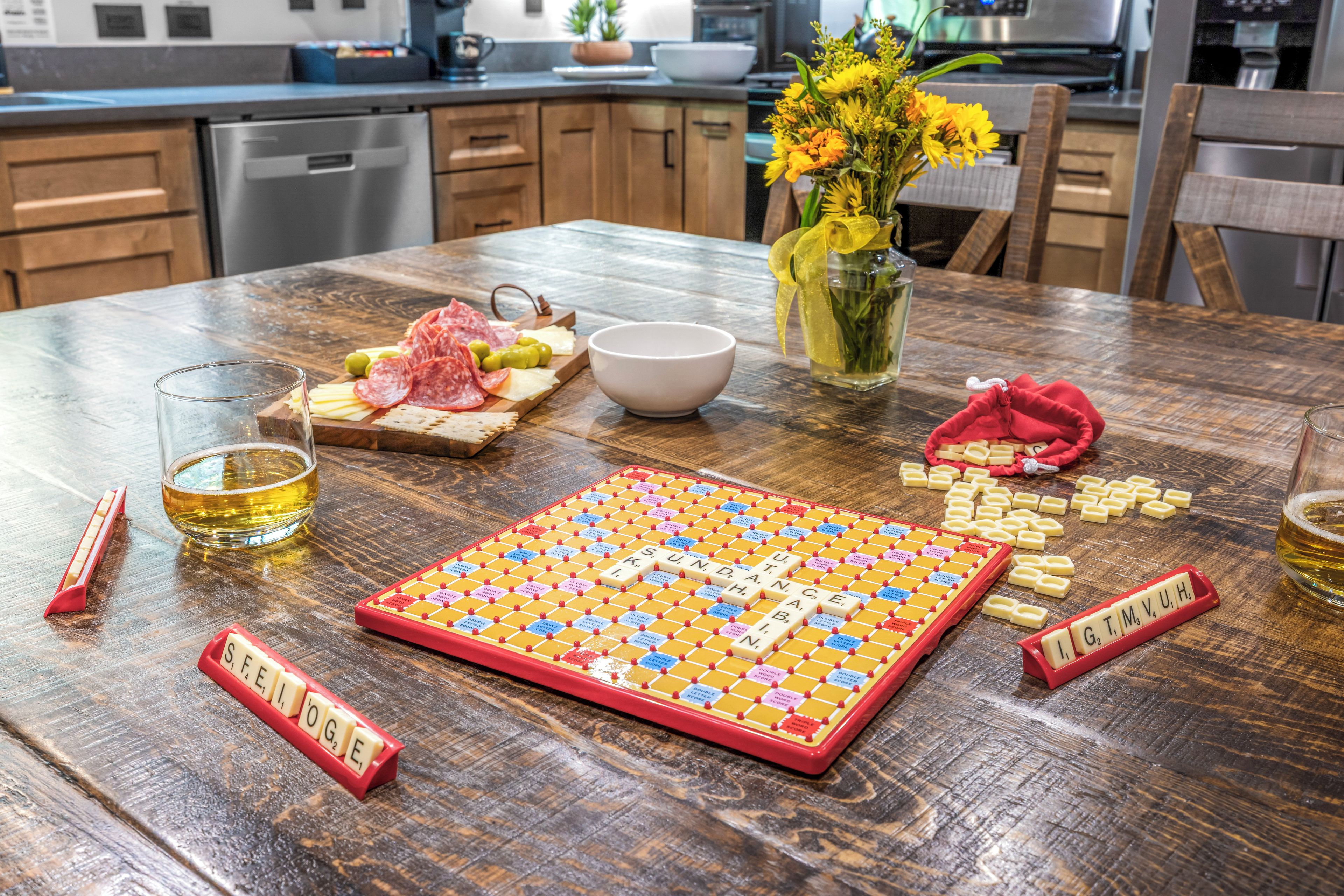 Una mesa de madera con un juego de Scrabble, un cuenco, una jarra de cerveza y un plato de comida.