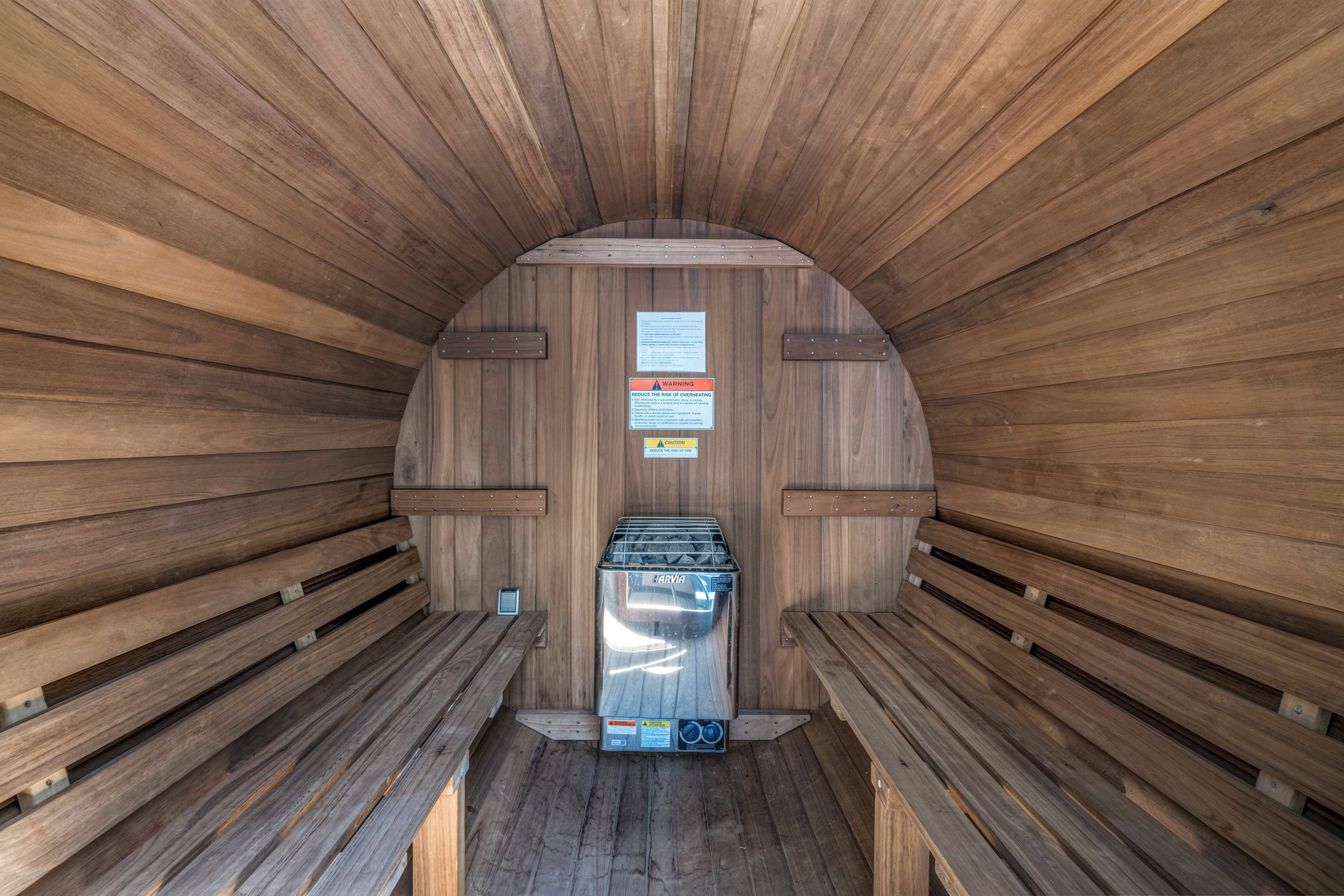 A sauna with wooden walls and benches, a heater, and safety warning signs.