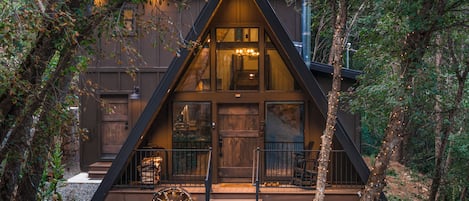 Una cabaña con techo triangular, fachada de madera y un porche con una carretilla.