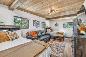 A spacious bedroom with a large bed, a sofa, and a desk area. There are multiple windows providing natural light and views of the outdoors. - Newly Remodeled A-Frame 5 min drive to Sundance (Sundance)