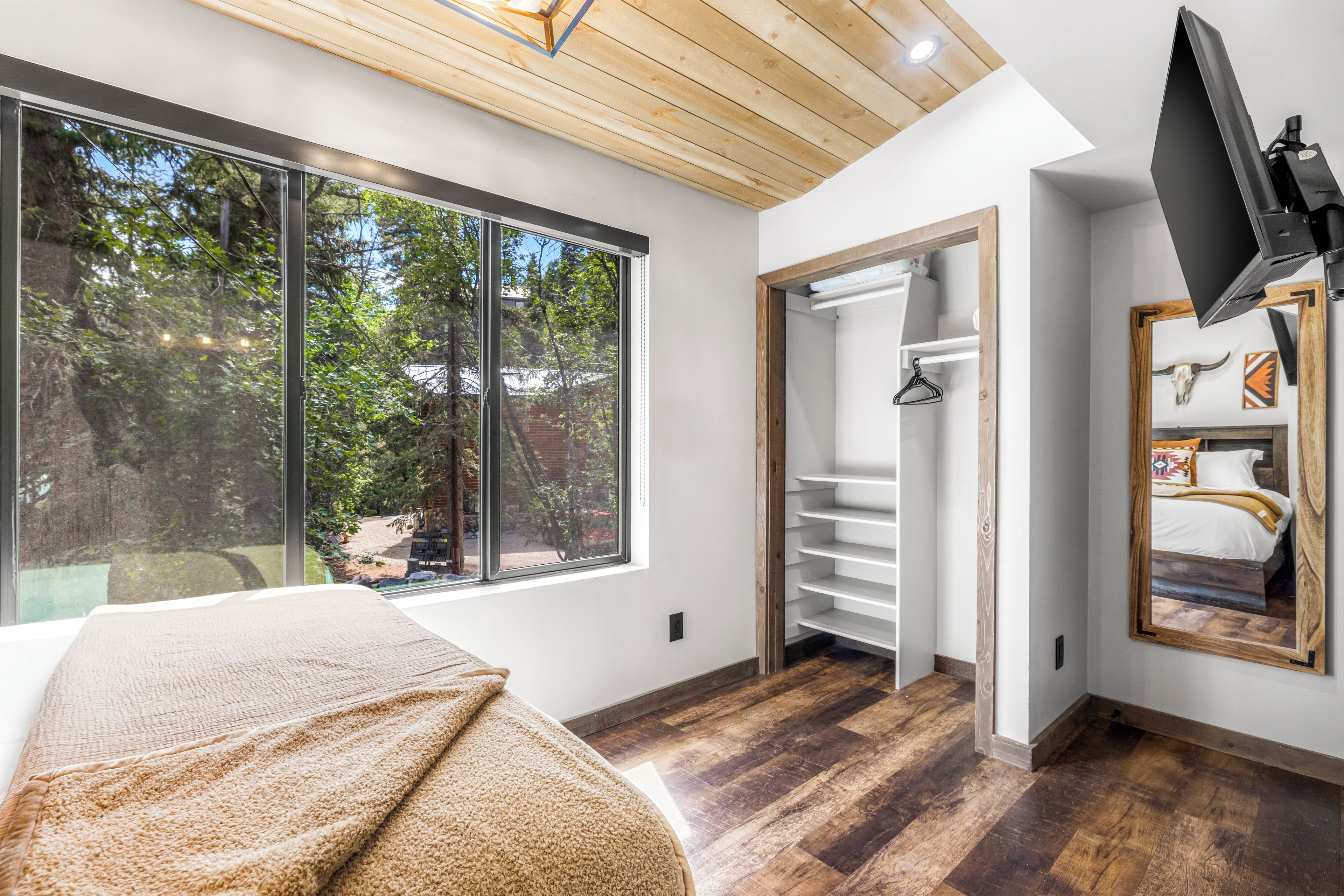 A bedroom with a large window, a bed, a wardrobe, and a TV mounted on the wall.