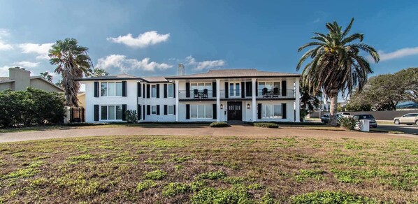 A two-story house with a balcony, a lawn, and a palm tree.