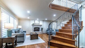 A spacious living room with a fireplace, a staircase with metal railings, and hardwood flooring. - Ocean Drive Grand Estate Sleeps 54 Pool (Corpus Christi)