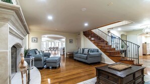 A spacious living room with a fireplace, a staircase, and a dining area in the background. - Ocean Drive Grand Estate Sleeps 54 Pool (Corpus Christi)