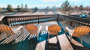 En træterrasse med fire Adirondack-stole, vendt mod en pool, omgivet af en træterrasse og udsigt til et bjerglandskab.