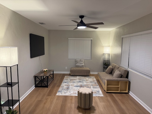 A living room with a ceiling fan, a flat-screen TV, a sofa, a coffee table, a side table, and a floor lamp.