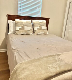 Un dormitorio con cama, dos almohadas, cabecera de madera y ventana con persianas.
