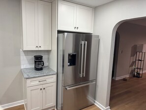 A kitchen with white cabinets, a stainless steel refrigerator, and a coffee maker on the countertop.