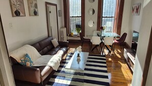A living room with a brown leather sofa, a striped rug, a glass coffee table, and a dining area with a glass table and chairs.