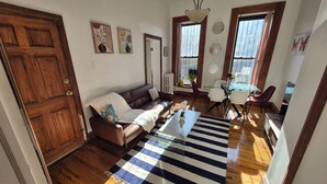 A living room with a brown leather sofa, a striped rug, and a dining area with a glass table and chairs.