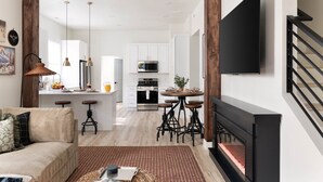 A modern living room with a fireplace, a sofa, and a kitchen in the background. - Ski Lodge, Ski Drop, Pickleball, HotTub, Sleeps 12 (South Salt Lake)